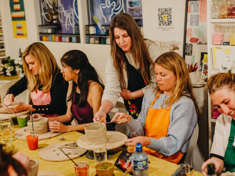 Three women are being taught handmade pottery by a ceramics teacher